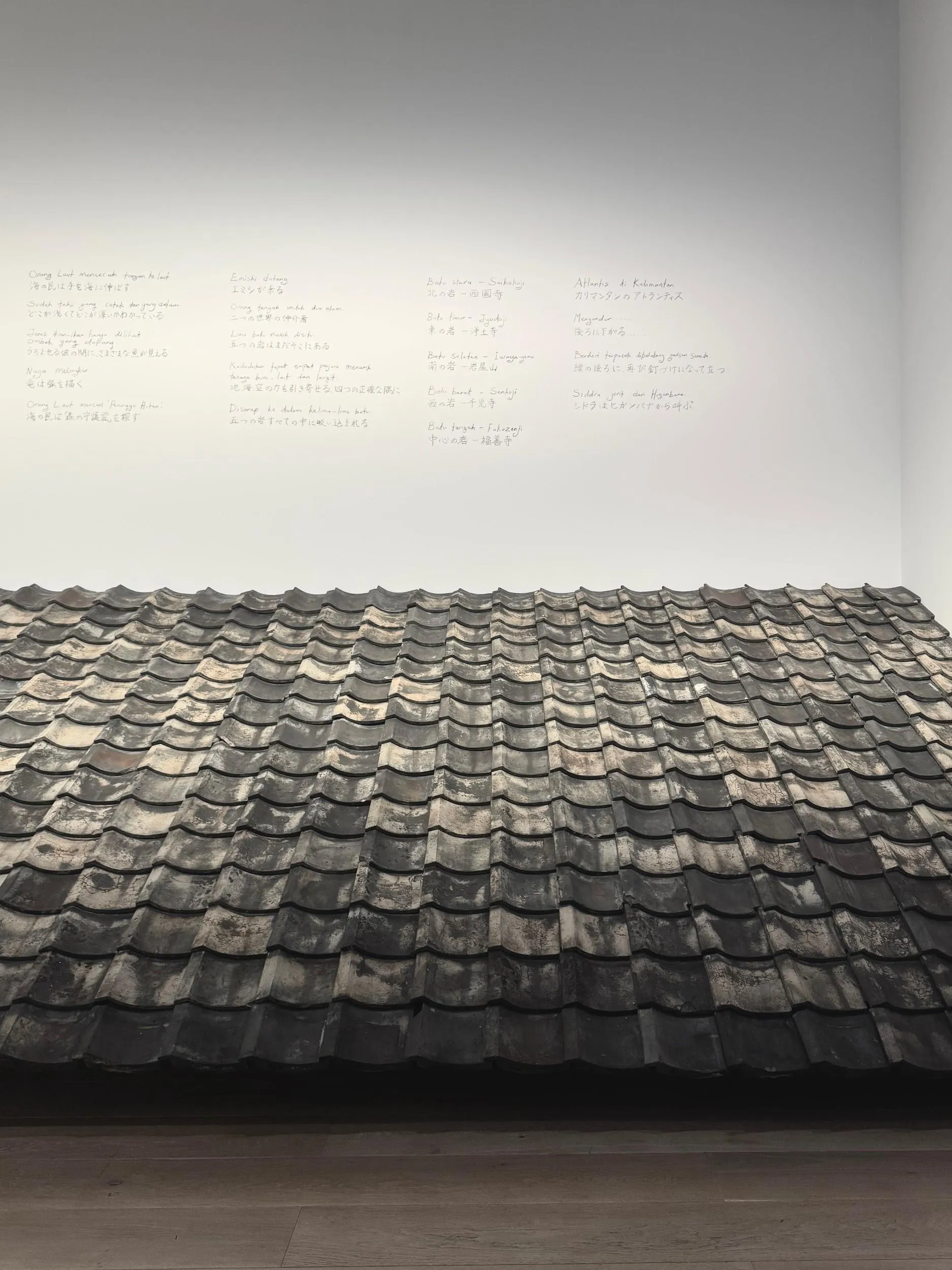 Yuko Mohri’s tiled roof segment beneath a wall of handwritten texts
